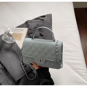 Detail of light grey quilted crossbody bag with silver chain and twist lock on white linen