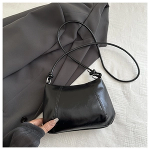 Detail of black glossy PU leather handbag with vertical stitching and slim strap