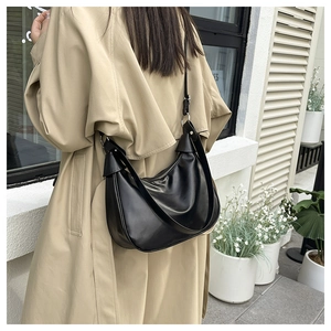 Black leather hobo crescent shoulder bag worn by a model with beige trench coat