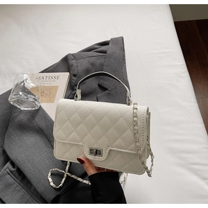 Close-up of quilted cream handbag with litchi texture, metal lock, and chain strap
