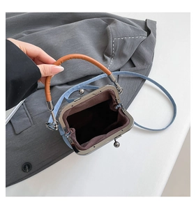 Detail view of denim kiss-lock bucket bag with brown leather handle and dark lining