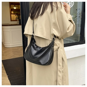 Outdoor shot of a black crescent shoulder bag with silver hardware on a beige coat
