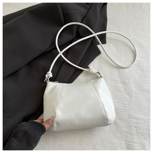 Detail of white leather crescent bag featuring minimalist knotted strap and vertical stitching