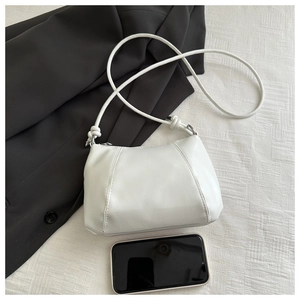 Size comparison of white leather bag next to a smartphone featuring knot strap details