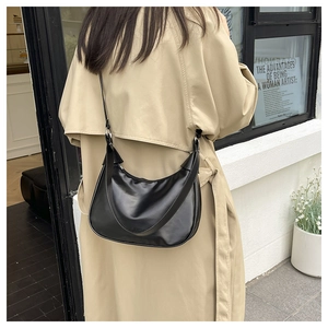 Close-up of black leather hobo crescent bag worn by model in beige trench coat