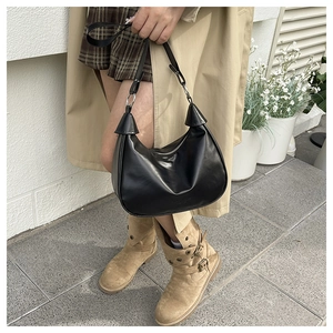 Detail of black glossy crescent bag with silver rings on a trench coat model