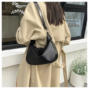 Street style shot of a black leather hobo bag worn with a beige trench coat
