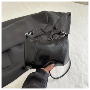 Detail of a black leather crescent handbag with a knotted handle and shoulder strap