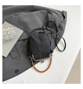 Detail of dark denim bucket bag with kiss-lock clasp, brown handle and silver hardware