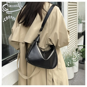 Détail d'un sac hobo en similicuir noir porté avec un trench-coat beige élégant