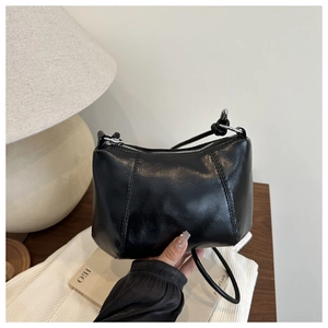 Glossy black PU leather crossbody bag with zipper and thin strap on a wooden desk