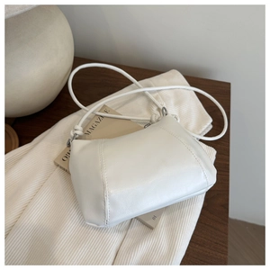 Detail of minimalist cream leather crossbody bag featuring slim shoulder straps on wood surface