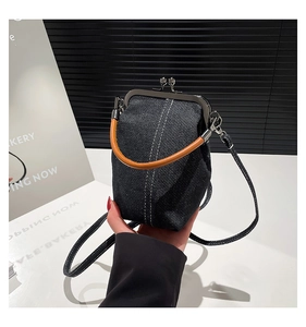 Detail of blue denim bucket bag with metal clasp, white stitching and brown leather handle