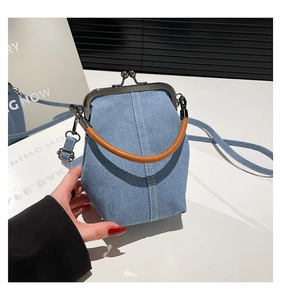 Detail of blue denim bucket bag with brown round handle and metal kiss-lock closure