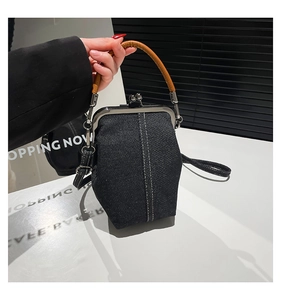 Detail of black denim bucket bag with metal clasp, contrast stitching, and leather handle