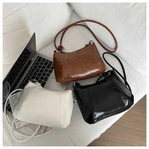Close-up of minimalist faux leather shoulder bags in white, brown, and black with knot detail