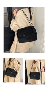Detail of minimalist black leather underarm bag with metal chain strap and white text logo