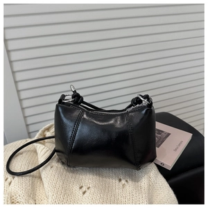 Close-up of black glossy mini handbag with silver hardware on knitted sweater