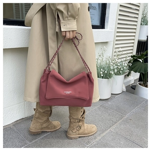 Chic rose pink shoulder bag with chain strap styled with a trench coat on a city street