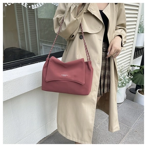 Detail of rose pink leather flap bag with metal chain strap worn on the shoulder