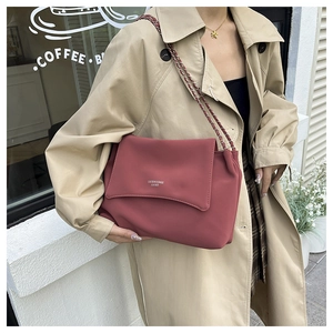 Detail of a brick red leather flap bag with gold chain strap in an urban cafe setting