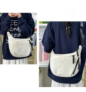 Detail of adjustable black nylon strap and zipper pocket on a white crescent crossbody bag