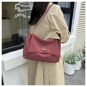 Fashionable dusty pink leather shoulder bag with chain strap worn with a stylish beige coat