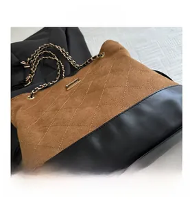 Detail of quilted brown suede and black leather stitching with gold chain strap