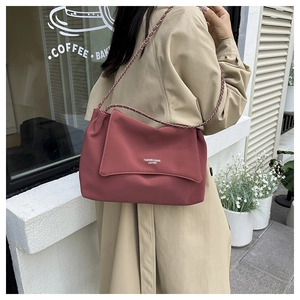Detail of red leather shoulder bag featuring a woven chain strap and minimalist logo