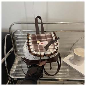 Détail du rabat à carreaux avec écusson cerise et nœud sur un petit sac à dos