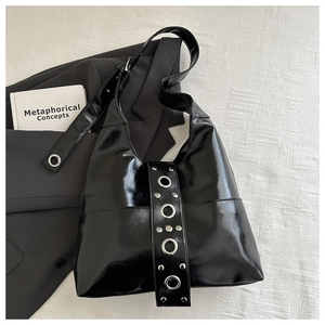 Detail of wide shoulder strap with silver metal grommets on a black patent leather tote bag