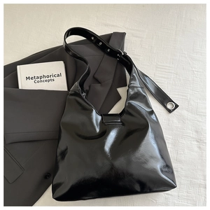 Close-up of shiny black patent leather shoulder bag with metallic buckle and silver eyelets