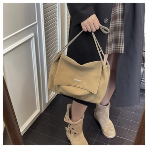 Detail of light khaki leather underarm bag with chain strap on a model in a black coat
