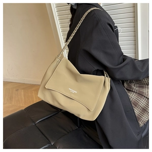 Detail of khaki leather shoulder bag with metal chain strap worn with black blazer