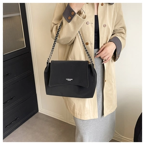 Detail of minimalist black chain shoulder bag with magnetic flap on a model outfit