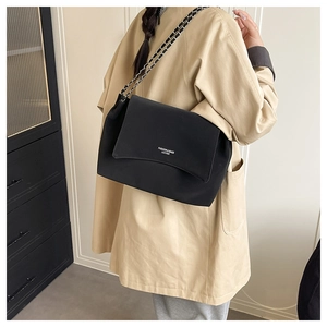 Detail of a black leather shoulder bag with white lettering and woven chain strap on a model