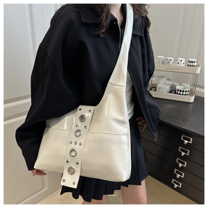 Detail of cream white patent leather hobo bag featuring decorative metal eyelet straps