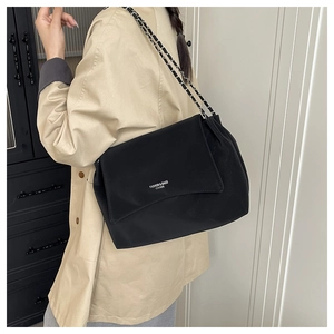 Detail showing the adjustable metal chain shoulder strap on a black minimalist shoulder bag