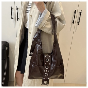 Detail of dark brown glossy hobo bag with silver rivets worn over a beige coat