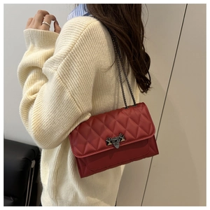 Detail shot of a red quilted crossbody bag with metal chain strap and luxury buckle