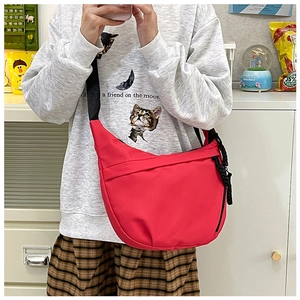 Detail of red nylon crescent crossbody bag with black strap and woven zipper pull
