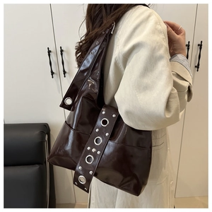Close-up of a dark brown glossy patent leather shoulder bag with silver metal eyelets