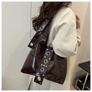Detail of vintage brown patent leather tote bag with large metal rivets worn on shoulder
