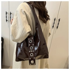 Model wearing dark brown glossy leather shoulder bag with metallic rivets and silver studs