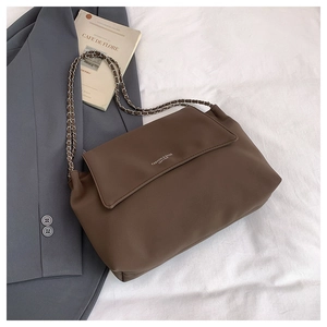 Detailed top view of a brown leather shoulder bag with gold chain strap on soft fabric