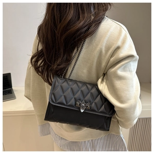 Detail of black quilted crossbody bag with metal heart buckle and stylish chain strap