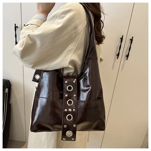 Close-up of shiny dark brown shoulder bag with silver eyelets and punk rivet details