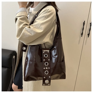 Detail of dark brown glossy leather shoulder bag with silver eyelets and metal studs