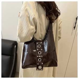 Detail of glossy brown patent leather bag with silver metal eyelets on the shoulder strap