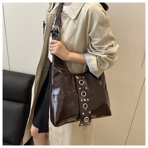Detailed close-up of a brown patent leather punk shoulder bag with silver eyelets and studs